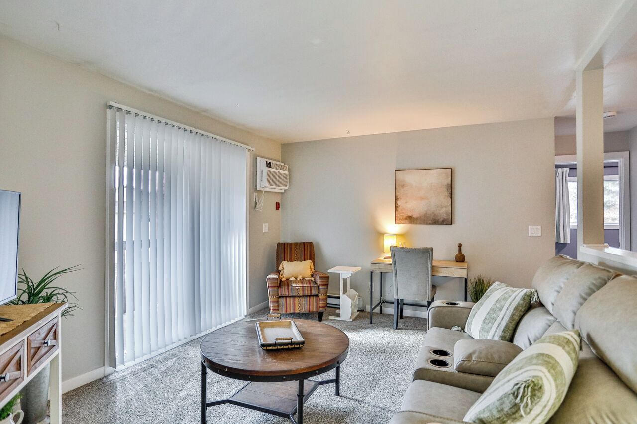 A living room with a sofa, a coffee table, a TV, a chair, a desk, and a lamp.