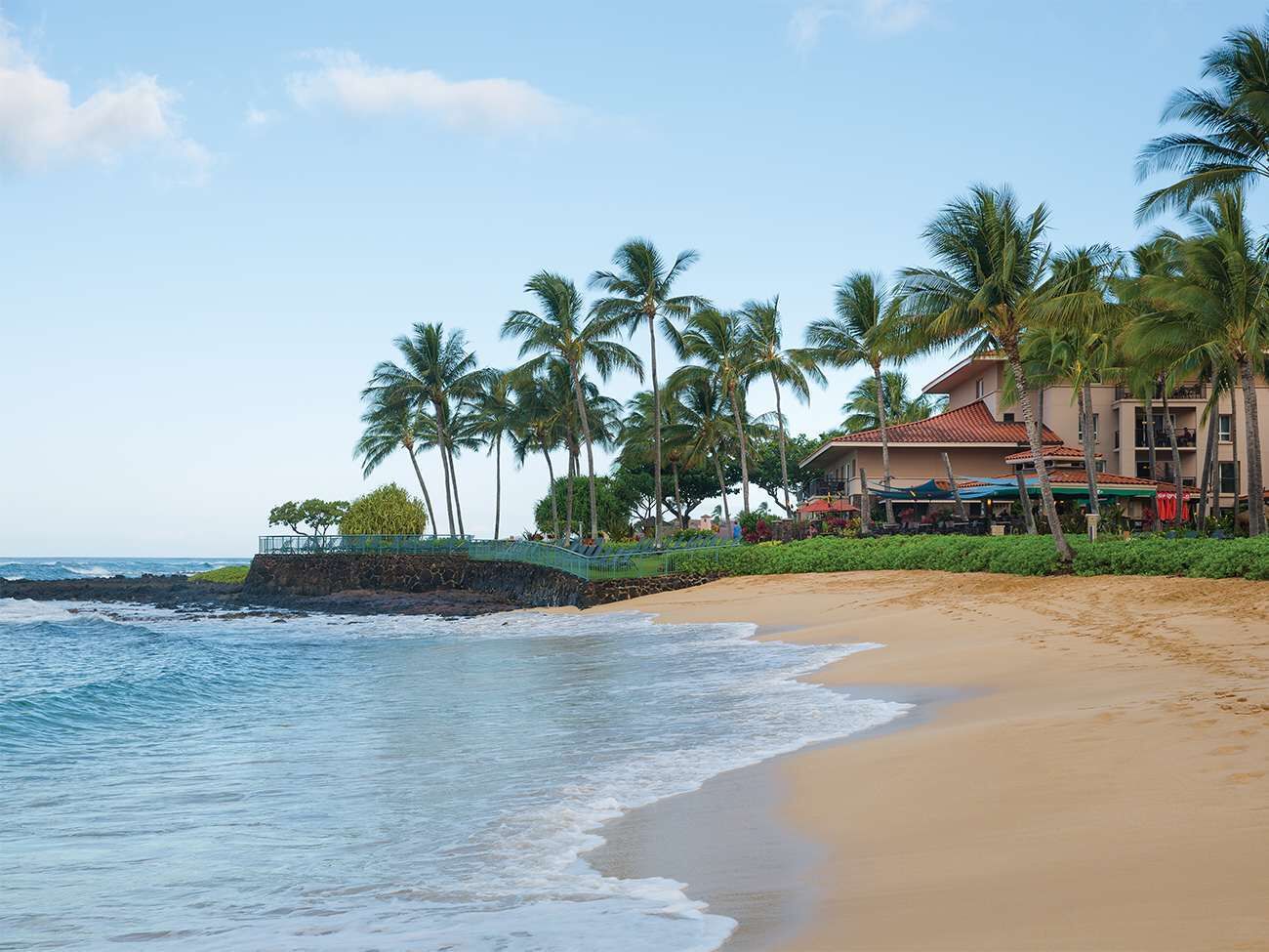 Ein Strand mit einem Hotel im Hintergrund, Palmen und Wellen.