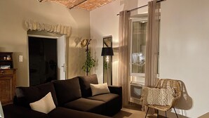 A living room with a dark brown sofa, a wicker chair, a lamp, and a door leading to another room.