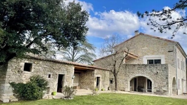 A stone building with a tiled roof, a small porch, and a grassy yard.