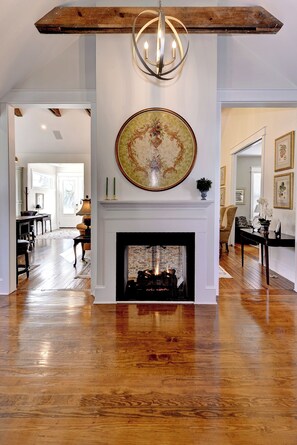 A spacious living area with a fireplace, wooden flooring, and a chandelier.