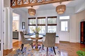 A dining area with a round table, two chairs, a vase with flowers, and a wooden ceiling beam.