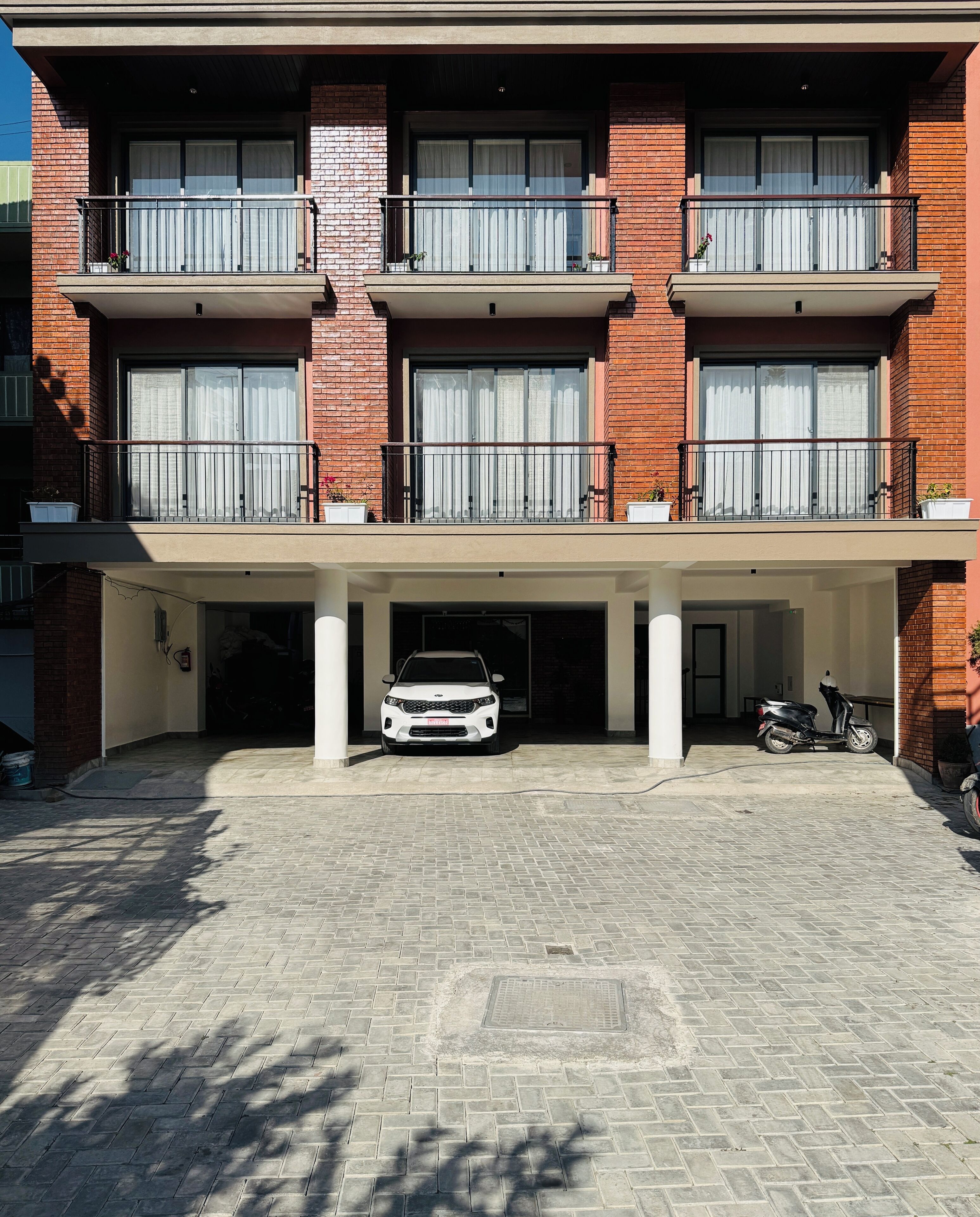 Un edificio de varios pisos con fachada de ladrillo, varios balcones y un área de estacionamiento techada con un coche blanco y una moto.