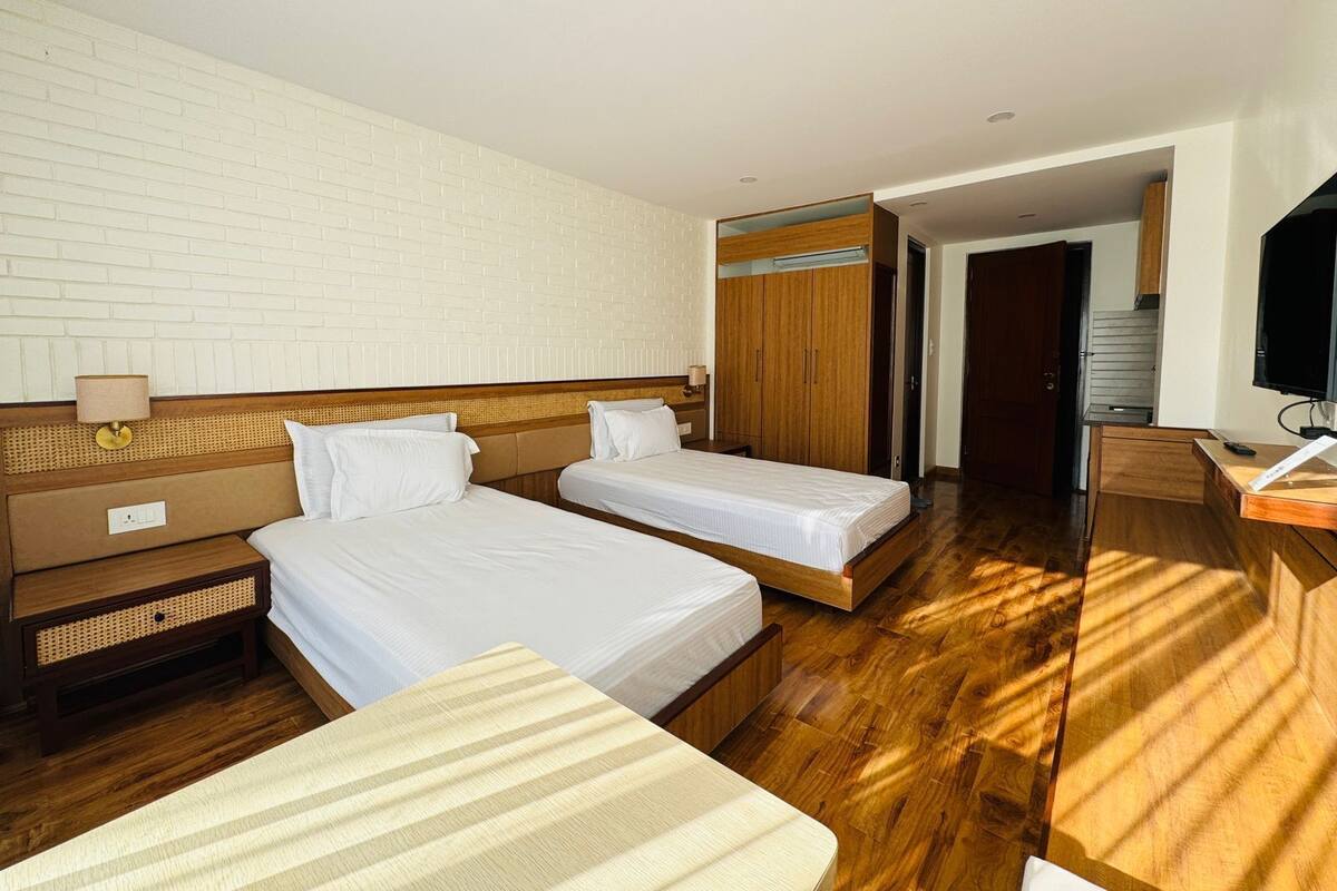 A hotel room with two single beds, a wooden desk, a TV, and a wardrobe.