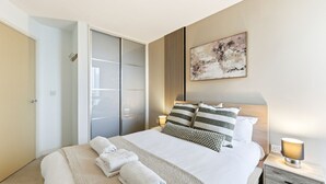 Une chambre à coucher moderne, avec un lit, des tables de chevet, une armoire et un tableau au mur.