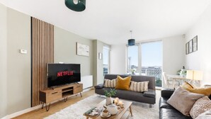 Un salon moderne doté d’un téléviseur à écran plat, d’un canapé, d’une table basse et offrant une vue sur la ville grâce à de grandes fenêtres.