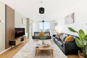 Ein modernes Wohnzimmer mit Flachbildfernseher, einer Couch, einem Couchtisch und einem großen Fenster.