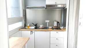Eine kleine Küche mit weißen Schränken, einer Edelstahl-Dunstabzugshaube, einer Holz Arbeitsplatte und zwei Hockern.