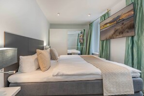 A modern hotel room with a large bed, a flat-screen TV mounted on the wall, and a view of a sunset over a beach. - Comfortable apartment in Villa Tanneck with terrace near the beach and center (Ahlbeck)