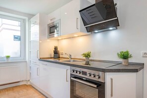 Une cuisine moderne avec des armoires blanches, un four à micro-ondes encastré, une cuisinière et un évier.
