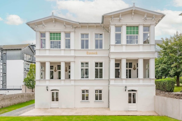 Un bâtiment blanc dont la façade porte l’inscription « Fanneck », avec de nombreuses fenêtres et une architecture symétrique.
