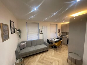 Een compacte woonruimte met een bank, eettafel, stoelen en een kitchenette.