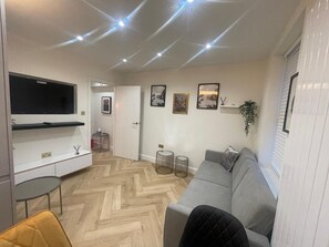 Een moderne woonkamer met een grijze bank, een aan de muur bevestigde televisie en een visgraatvloer.