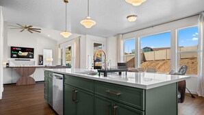 A modern kitchen with a large island, green cabinets, and a flat-screen TV displaying streaming services. - Roam Away From Home R4|Fire Pit |Office |Hot Tub (Mountain Green)
