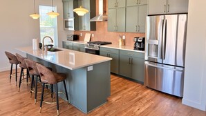A modern kitchen with a central island, stainless steel appliances, and green cabinetry. - Roam Away From Home R4|Fire Pit |Office |Hot Tub (Mountain Green)