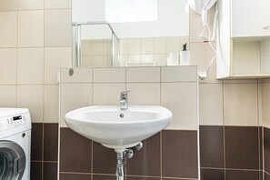 A bathroom with a white sink, a washing machine, and a mirror.
