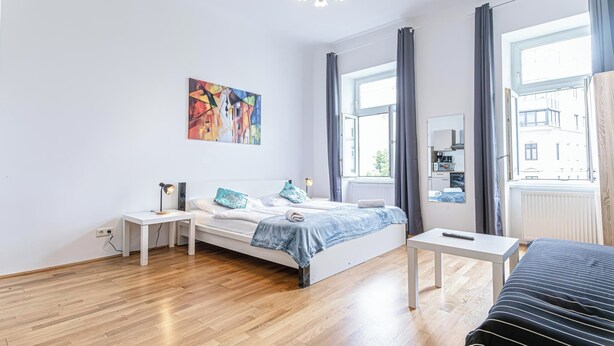 A modern bedroom with a bed, bedside tables, a desk, and a large window. - Comfy 2BR Flat Belvedere Vicinity (Vienna)