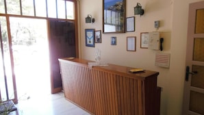 A reception area with a wooden counter, framed certificates, a framed photograph, and a wall-mounted phone. - Three Brothers Hotel (Aegina)