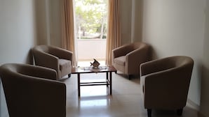 A living room with a central coffee table, two armchairs, a ceiling light, and a view through a large window. - Three Brothers Hotel (Aegina)