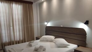 A modern hotel room with a large bed, wooden headboard, and bedside tables. - Three Brothers Hotel (Aegina)