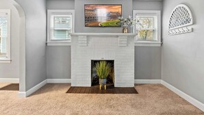 A room with a white brick fireplace, a mounted TV, and a decorative lattice on the wall. - Your perfect getaway| 1 mile from Churchill Downs! (Louisville)