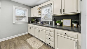 A kitchen with white cabinets, a black countertop, and a window with blinds. - Your perfect getaway| 1 mile from Churchill Downs! (Louisville)