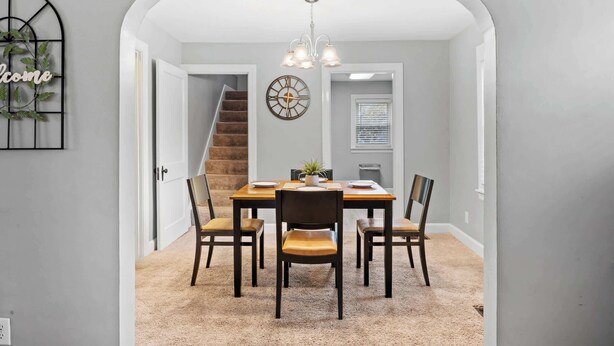 A dining area with a wooden table and chairs, a chandelier, and a clock on the wall. - Your perfect getaway| 1 mile from Churchill Downs! (Louisville)