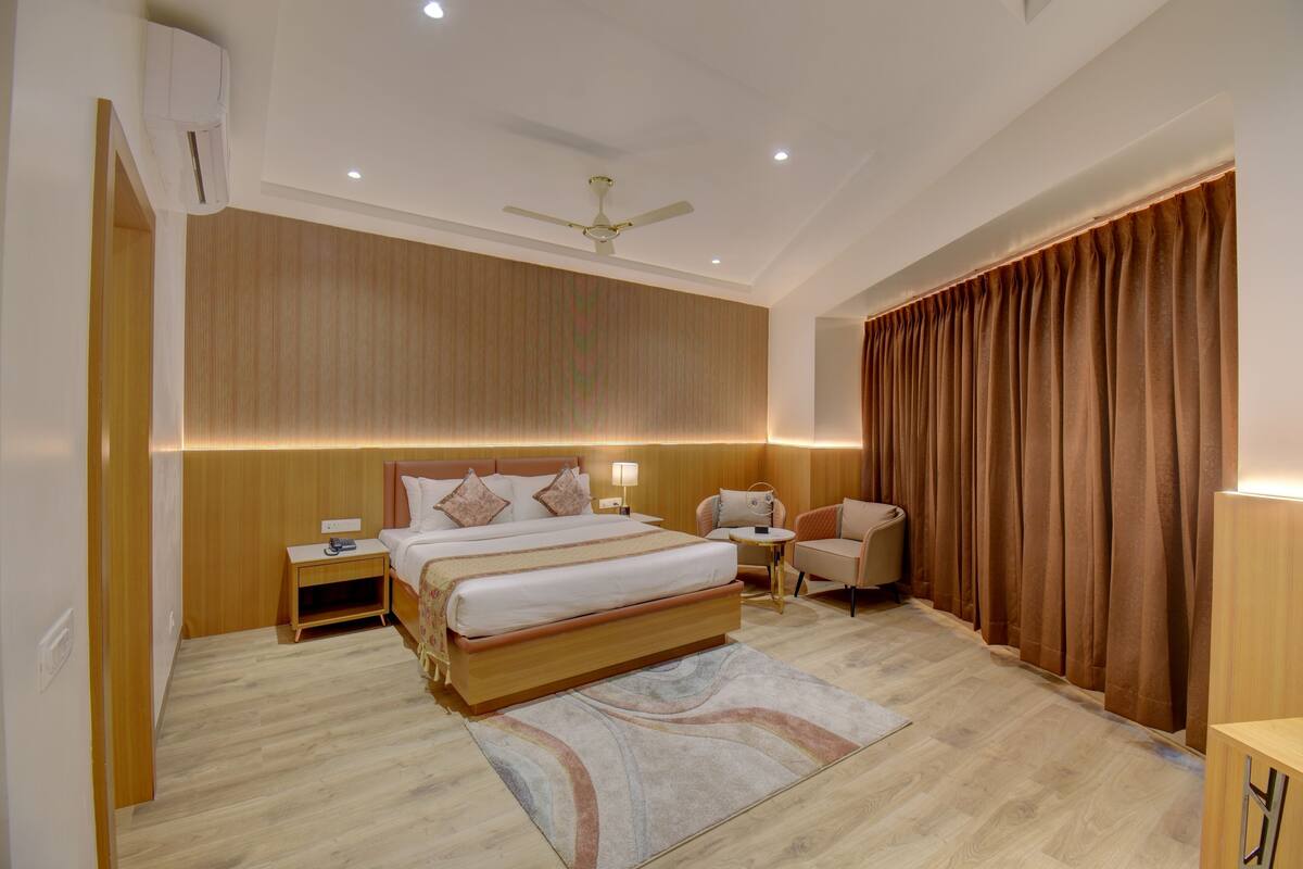 Una habitación de hotel moderna con una cama grande, un ventilador de techo, una mesita de noche con lámpara, una pequeña mesa auxiliar y una silla.