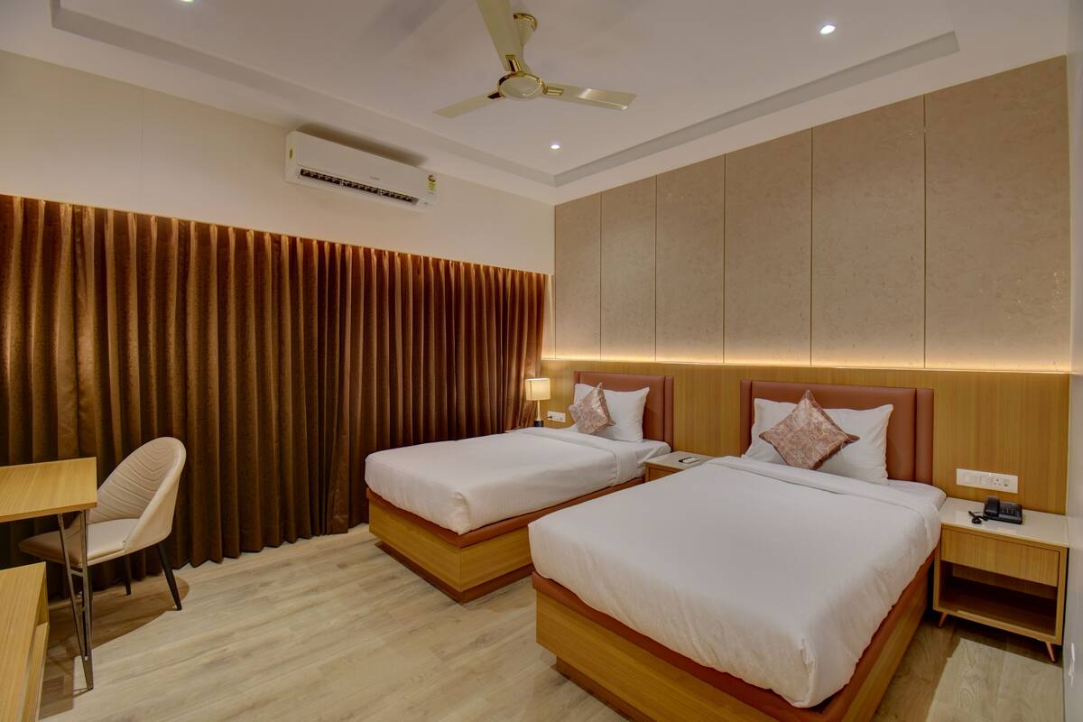 Habitación de hotel con dos camas, un escritorio, una silla, aire acondicionado y ventilador de techo.