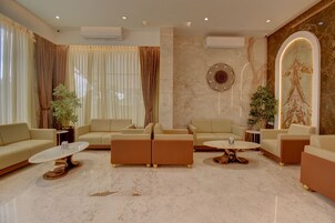 Una sala de estar moderna con sofás color beige, suelo de mármol y plantas decorativas.
