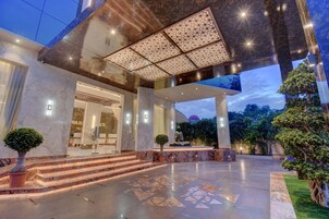 Una entrada de hotel moderna con fachada de mármol, un amplio alero y un área exterior bien iluminada.