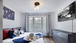 Une chambre à coucher avec un lit, une commode, une fenêtre et un tableau accroché au mur.