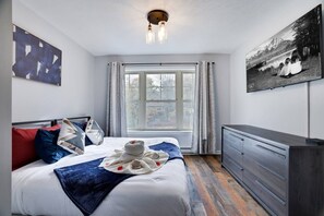 A bedroom with a bed, a dresser, a window, and a painting on the wall.