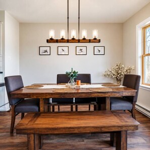 A dining room with a wooden table, black chairs, a bench, a chandelier, framed artwork, and a vase with flowers.