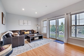 A modern living room with a dark leather sofa, a coffee table, and a large sliding glass door leading to a driveway. - Mountain Chalet| Ski, Hike, & Explore (Tannersville)