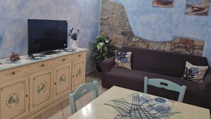 Una sala de estar con televisor, sofá, mesa de comedor y un detalle decorativo en la pared.