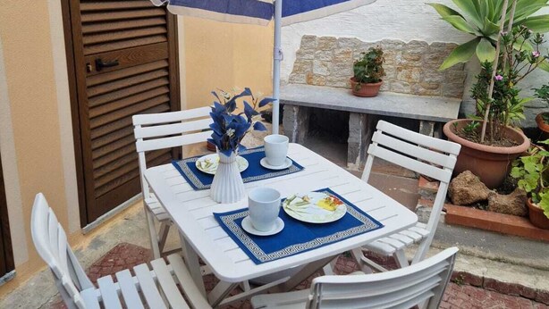 Un patio con una mesa para dos, una sombrilla y plantas en macetas.