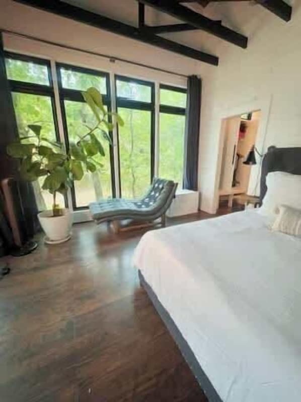 A bedroom with a large bed, a potted plant, and a chair by a window.