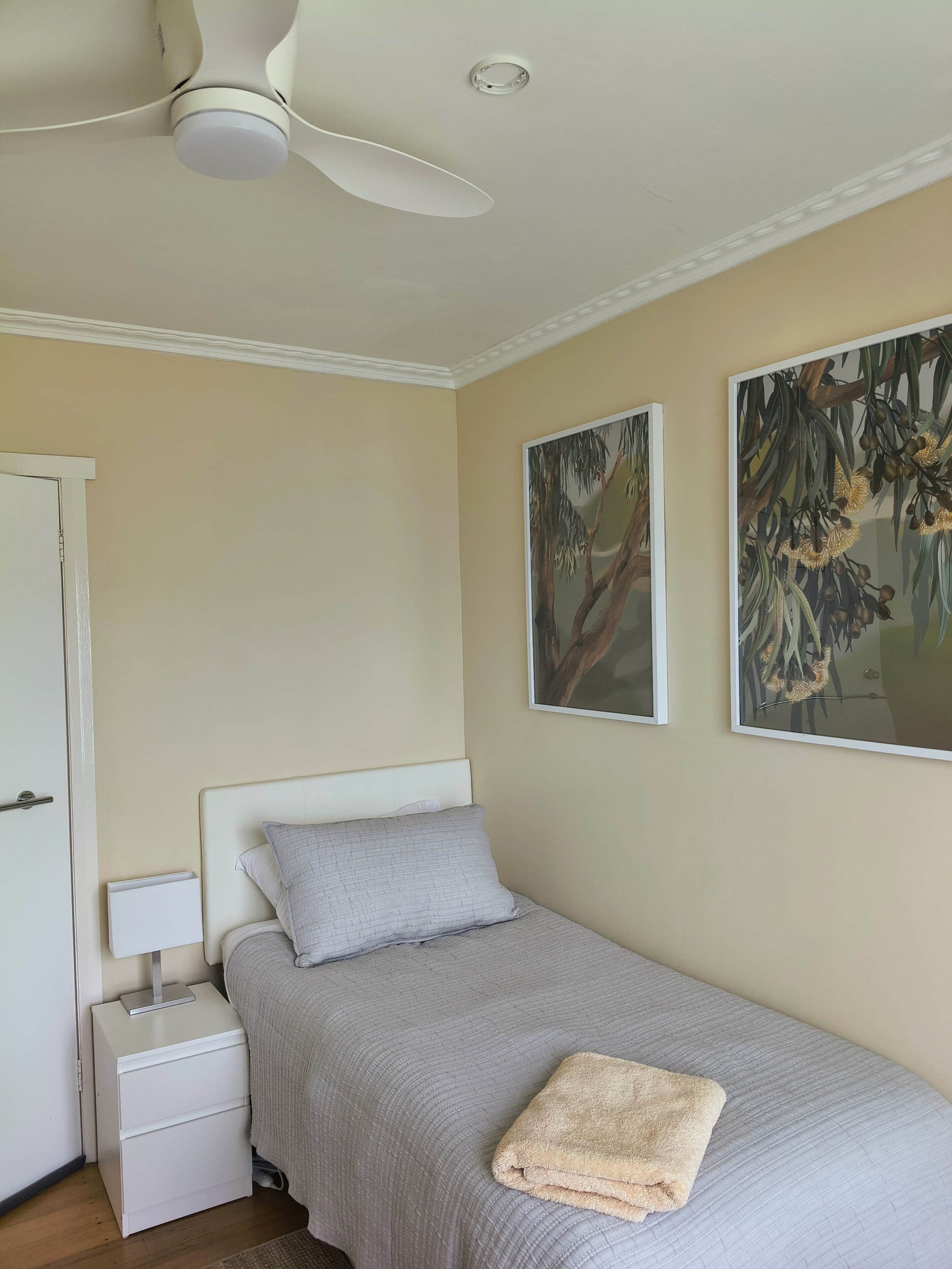 Een slaapkamer met een bed, een nachtkastje, een plafondventilator en twee aan de muur hangende schilderijen.