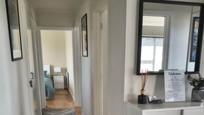 A hallway with a patterned rug, a reception desk with a welcome sign, and a bed with a blue headboard in the background.