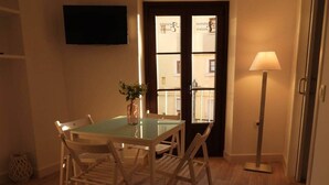 Un comedor con una mesa de vidrio y sillas blancas, un jarrón con flores, una lámpara de pie y una puerta con paneles de vidrio.