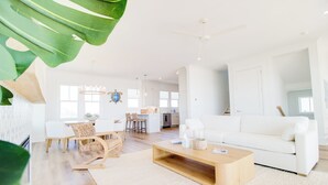 A spacious living room with a white sofa, wooden coffee table, and a dining area with a white table and wicker chairs. - New Oceanfront Home | Private Beach Access (Topsail Beach)