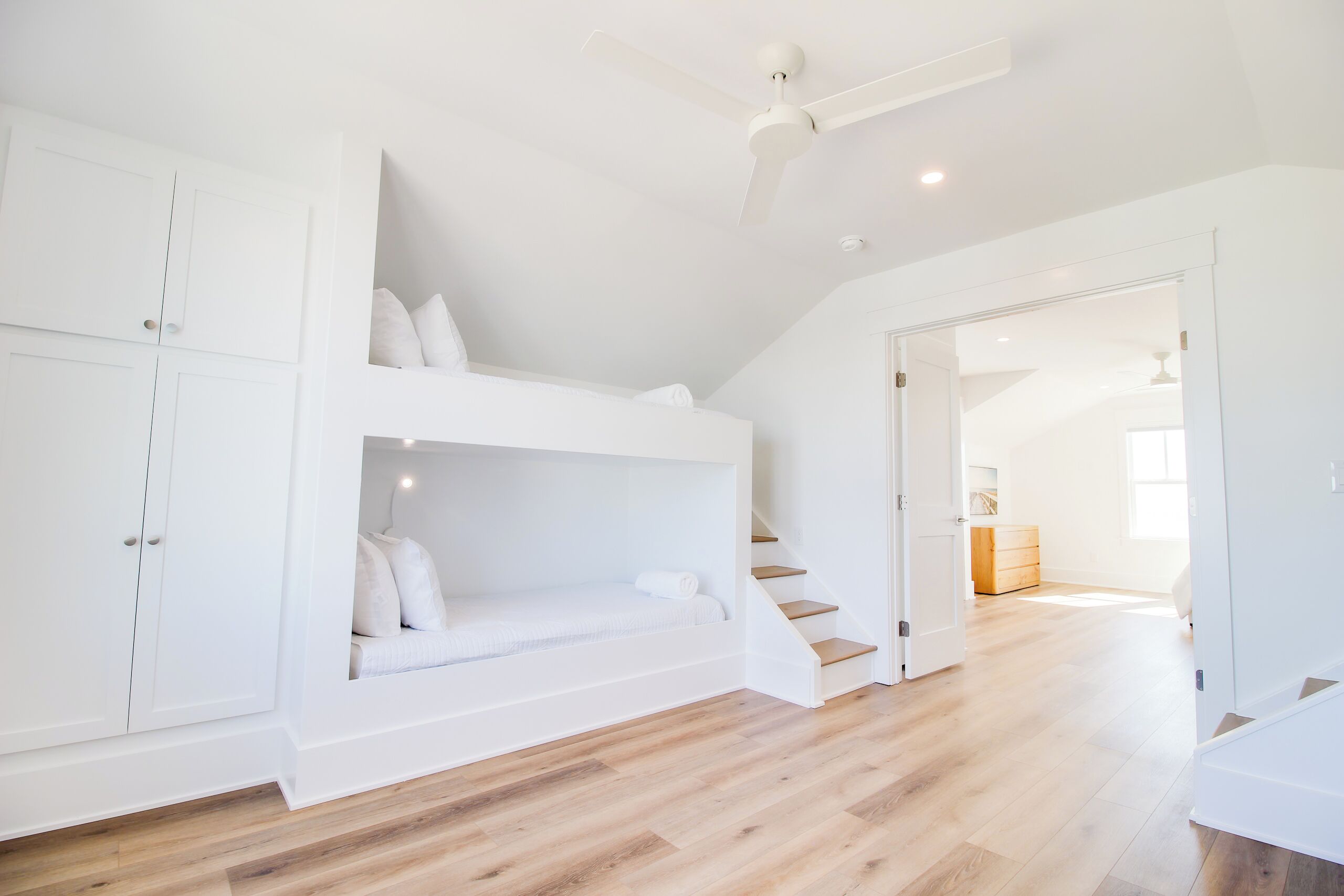 A bedroom with a bunk bed, a wardrobe, and a staircase leading to another room.