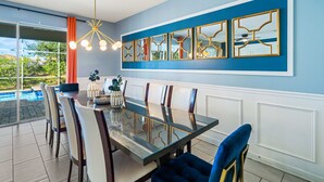 Ein Essbereich mit einem Tisch mit Glasplatte, weißen gepolsterten Stühlen und einer blauen Wand mit goldfarbenen Spiegeln.