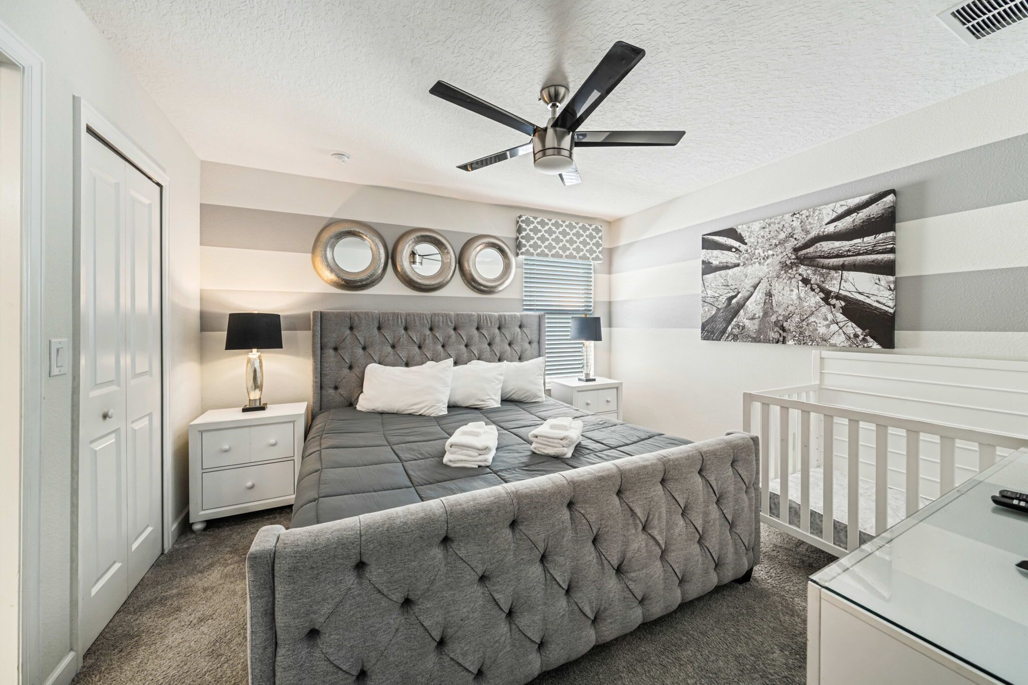 A bedroom with a tufted headboard, a bed with pillows, a nightstand with a lamp, a ceiling fan, and a wall-mounted artwork.