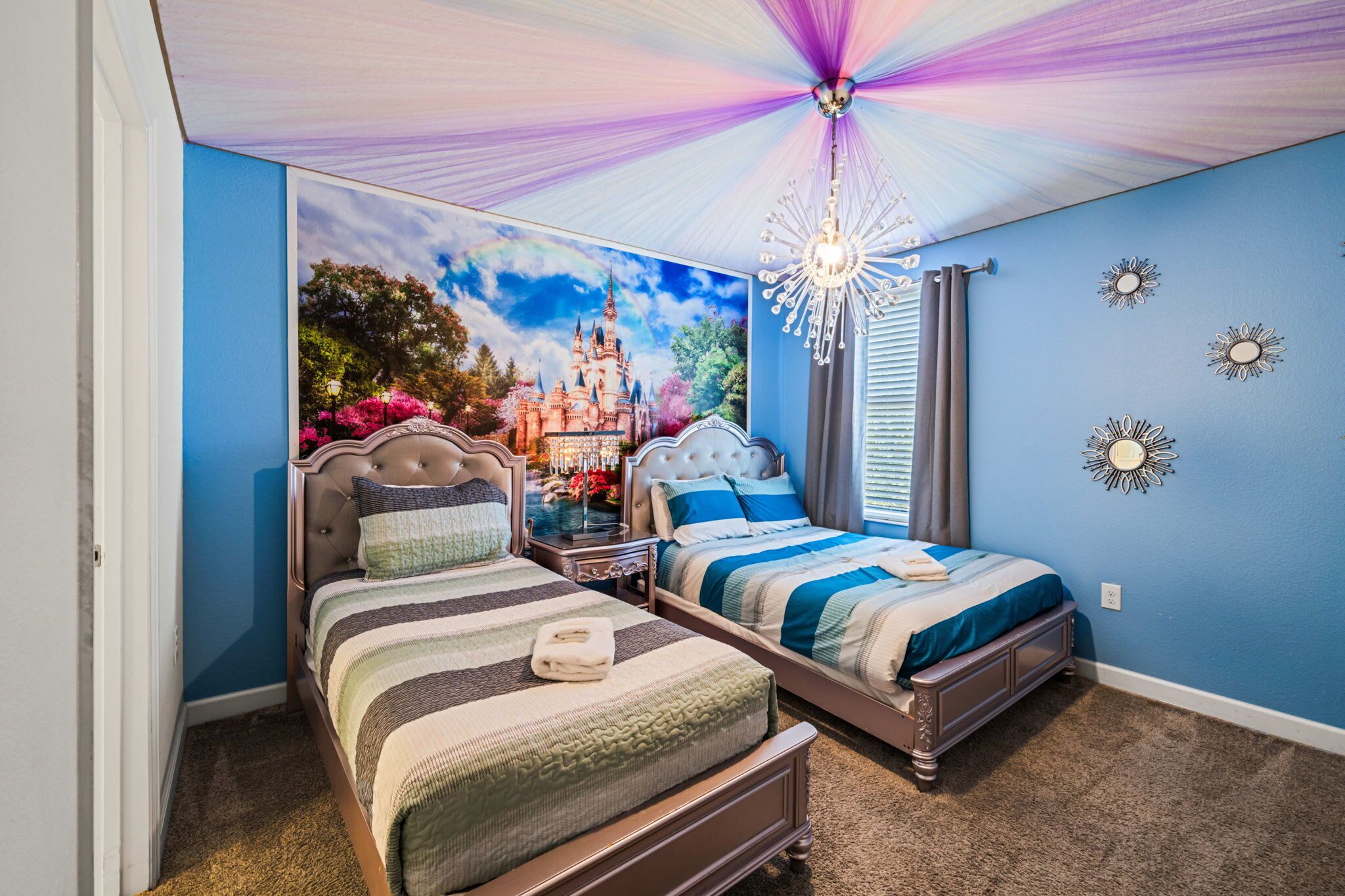 A bedroom with two beds, a chandelier, and a castle-themed wall mural.