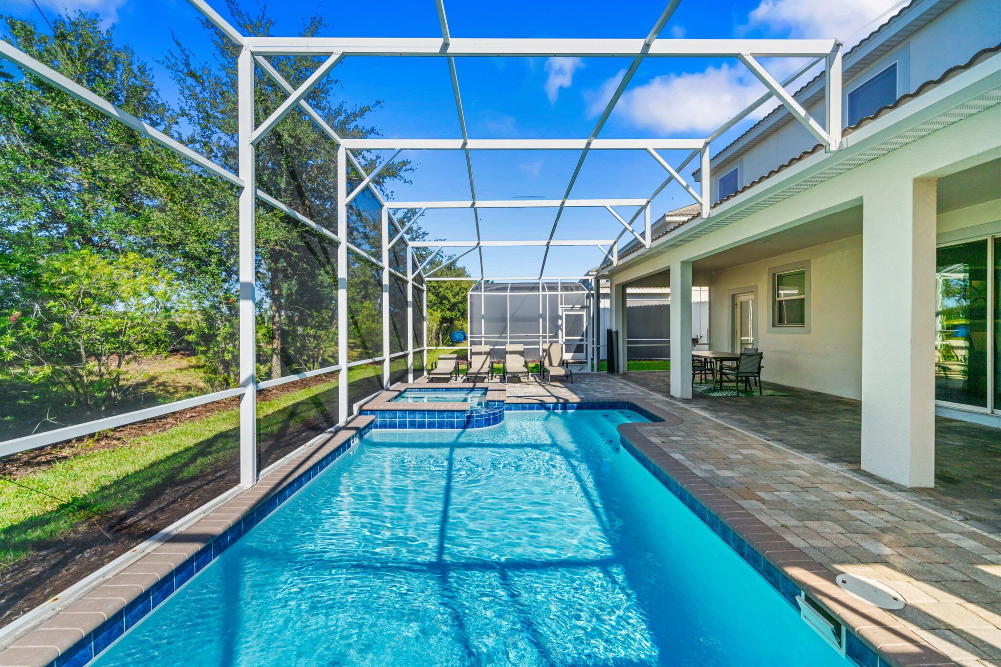 A swimming pool with a covered area, surrounded by a white fence, and a patio with outdoor furniture.