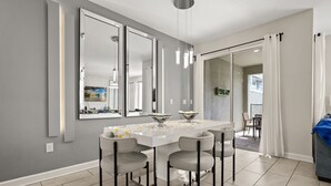 A modern dining area with a white table, four grey chairs, and three large mirrors on the wall.