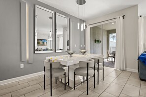 A modern dining area with a white table, four grey chairs, and three large mirrors on the wall.