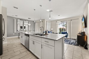 Une cuisine moderne dotée d’un grand îlot central, d’appareils électroménagers en acier inoxydable et de luminaires suspendus.